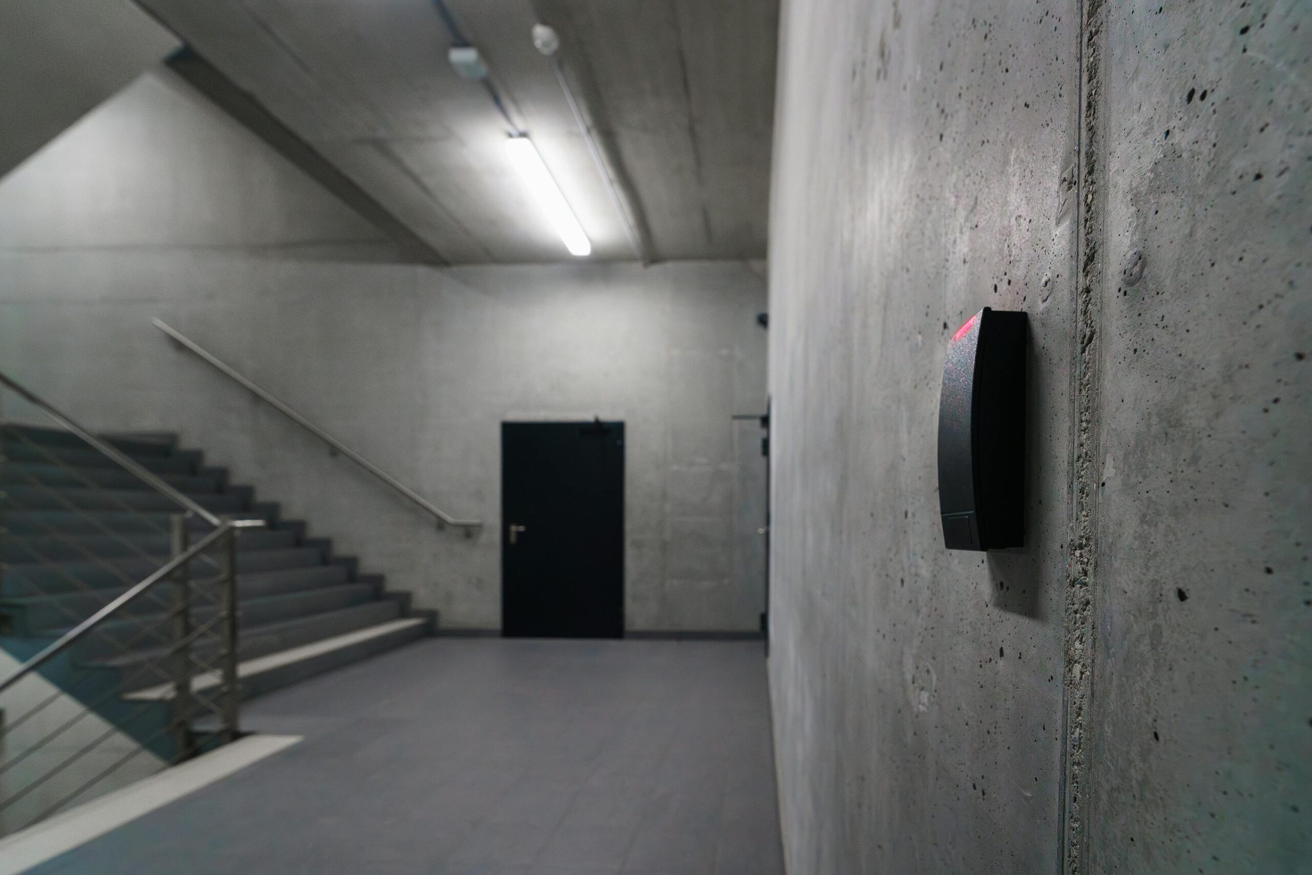 Minimalist concrete staircase with security device in office building corridor.